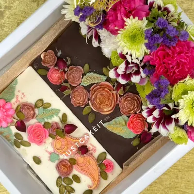 This 'Bloom with Gratitude' hamper features two artisanal chocolate bars, one white and one dark, both hand-painted with edible floral designs. It's paired with a bouquet of fresh, exotic flowers.