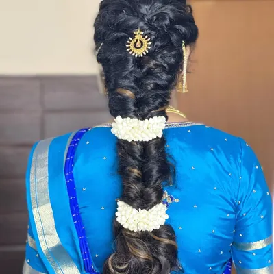 A detailed view of a beautiful, thick fishtail braid, accented with jasmine flowers and a traditional sun-shaped hair accessory. This hairstyle is perfect for a classic South Indian look.