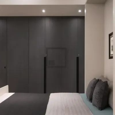 Here is an example of a floor-to-ceiling wardrobe in a dark grey finish that creates a calm, minimalist bedroom. The design features handleless doors for a clean look and a recessed niche for a television, perfectly integrating storage and media.