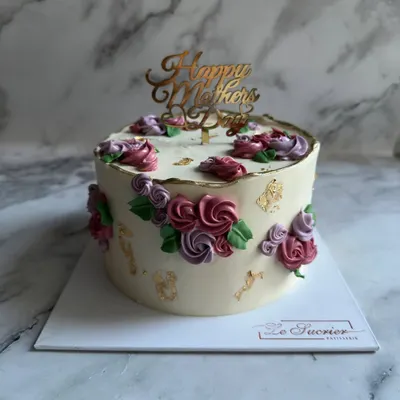 This elegant Mother's Day cake is decorated with delicate, hand-piped buttercream flowers in shades of pink and purple, finished with a touch of edible gold leaf for a luxurious feel.