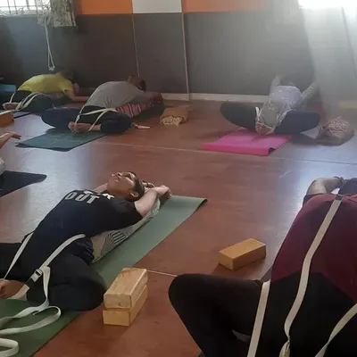 A class engaged in Supta Baddha Konasana (Reclining Bound Angle Pose) using straps. This restorative yoga pose helps to open the hips and chest gently with full support from props.