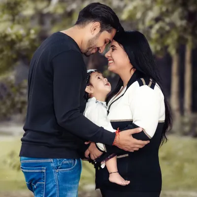 A beautiful, intimate family portrait taken outdoors. The focus is on the loving gaze between the parents and their baby, creating a timeless image of connection.