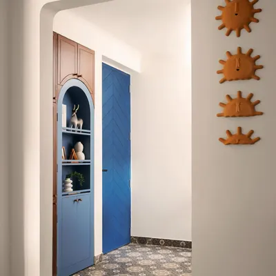 The entryway sets a playful and welcoming tone. A bold, chevron-patterned blue door opens to a foyer with patterned Moroccan floor tiles and a custom arched storage unit that combines open shelving with concealed cabinets.