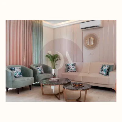 This living room showcases several custom pieces, including the pastel green armchairs and the nested marble-top coffee tables. Every piece is designed to complement the overall aesthetic of comfortable luxury.