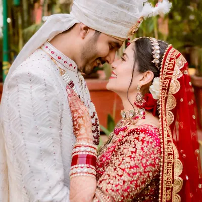 An intimate moment between the bride and groom, their foreheads touching in a gesture of pure affection. The soft lighting highlights their joyful expressions and the intricate details of their wedding attire.
