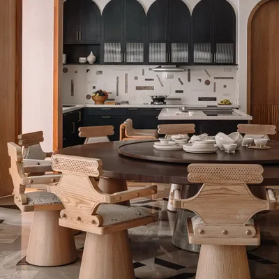 The dining room at Rehethaan, featuring impressive 'Kingpin' swivel chairs around a large circular table. The space opens up to the kitchen through a large, wood-framed archway.