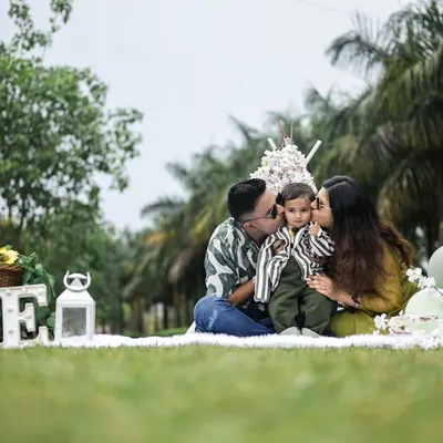 A beautiful family portrait during an outdoor first birthday session. The parents share a kiss with their son, creating a loving and warm memory in a picturesque park setting.