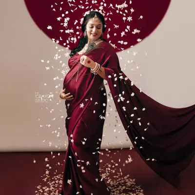 The flow of a beautiful red saree and a shower of petals create a sense of movement and celebration. This full length portrait captures the grace and power of the mother to be.
