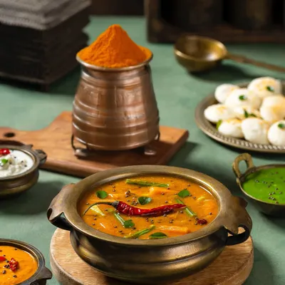 A traditional South Indian spread featuring sambar, idli, and chutneys for Rakesh Masala. The styling with brass and copper utensils creates an authentic, rustic ambiance.