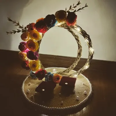 This is an engagement ring platter I designed for a client's special moment. It features two intertwined rings decorated with fairy lights and colourful paper flowers, creating a beautifully lit and romantic display for the exchange of rings.