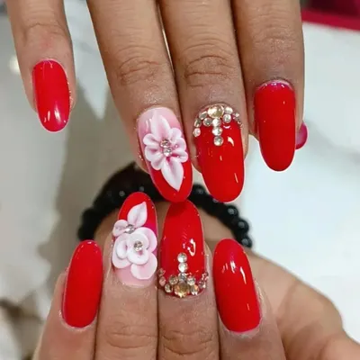 A bold and glamorous set featuring bright red nails, 3D sculpted flowers, and a full accent nail covered in sparkling rhinestones.