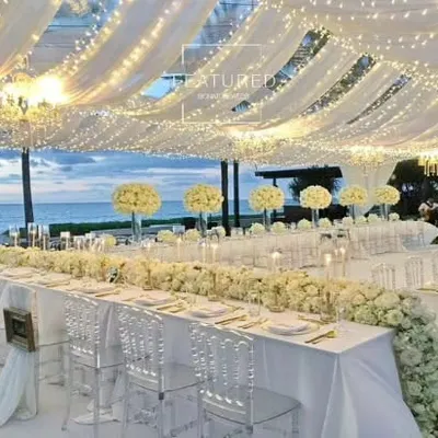 This all-white dining setup by the sea is the definition of elegance and is perfect for an exclusive corporate retreat or VIP dinner. The flowing drapery, fairy lights, and transparent chairs create a clean, sophisticated, and unforgettable ambiance.