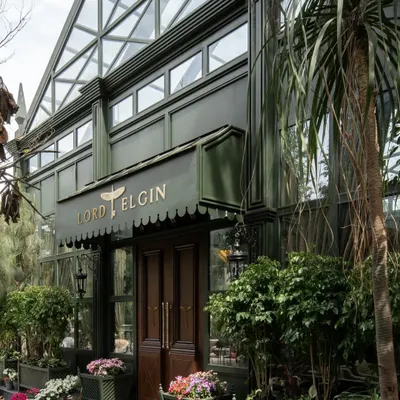 The exterior of the Lord Elgin Glasshouse, a striking green structure surrounded by vibrant flowers. The design immediately establishes the brand's identity as a lush, garden-like escape.