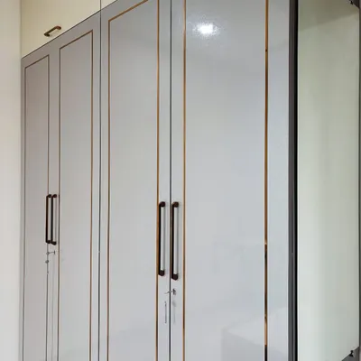 A sleek, modern wardrobe in a grey high-gloss finish with elegant gold inlay. This design includes a full-length mirror integrated into the side of the unit to save wall space.