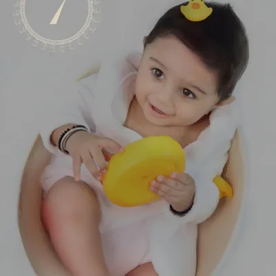 A happy baby in a little white bathrobe enjoys bath time play, holding a bright yellow rubber duck.
