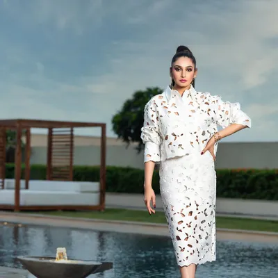 A high-fashion editorial photograph taken for a magazine cover. The composition places the model as a strong, central figure against the clean lines of the poolside location, emphasizing the unique laser-cut design of the white two-piece outfit.