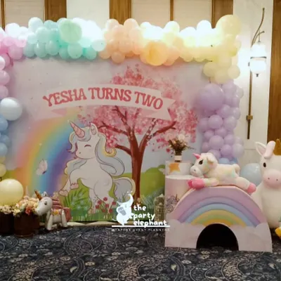 The complete unicorn party setup for Yesha's second birthday. This wide shot shows the main backdrop, pastel balloon garland, rainbow props, and adorable unicorn figures that create a whimsical atmosphere.