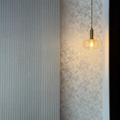 This wall’s got more lines than your ex during arguments. A close-up of a textured wall with vertical fluting next to a patterned wallpaper, lit by a single pendant.