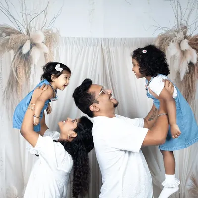 A fun and energetic family photo with parents lifting their two young daughters in the air, all smiling and laughing.