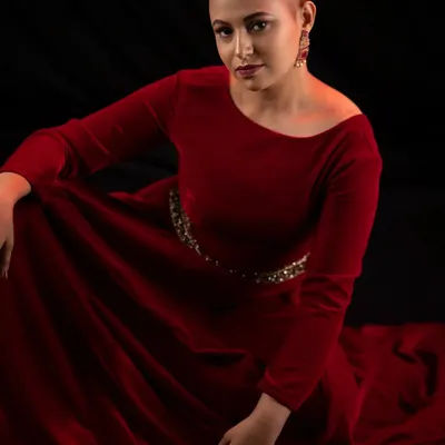 Bald, bold, and beautiful. This look is all about empowerment, featuring a strong, confident pose in a rich red velvet dress. The makeup is kept classic to let her powerful presence shine.