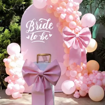 A closer look at a popular 'Bride to be' setup. The clean white arch provides a perfect canvas for the pretty pink balloon garland and statement bow, creating a beautiful focal point for photos.