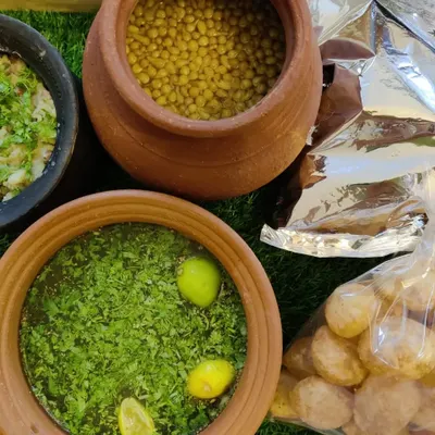 A close-up of our Pani Puri components, showing the spiced water (pani) in an earthen pot, boondi, and a bag of crispy, hollow puris.