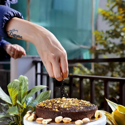 A lifestyle action shot of a hand sprinkling nuts on a freshly baked cake, adding a human element and a sense of freshness to the image.