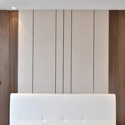 A complete bedroom solution where the wall itself is the headboard. This design features a mix of dark fluted wood, a central light wood panel, and a comfortable upholstered section, with integrated switches and designer lights.