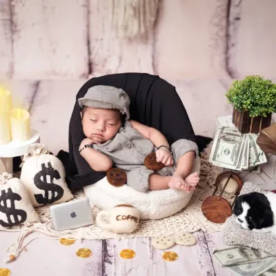 Meet the "Boss Baby"! This little one is styled in a grey outfit and cap, surrounded by props like money bags, a mini laptop, and a coffee mug.