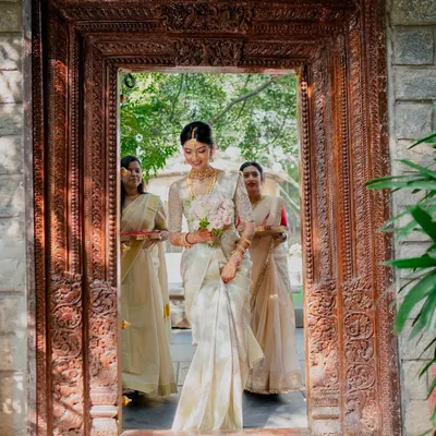 A radiant bride making her entrance at a day wedding, her soft ivory sari perfectly complementing the natural light and heritage venue.