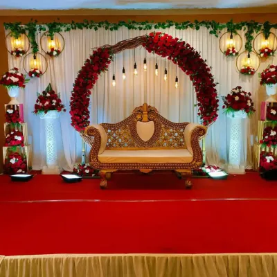 A stunning engagement stage with a circular arch of red roses, hanging lights, and a vintage gold sofa. This design is both modern and elegant.