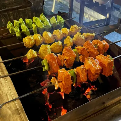 Who can resist the aroma of a sizzling barbecue? Here are skewers of Paneer Tikka and other marinated vegetables grilling over hot coals, getting that perfect smoky char.