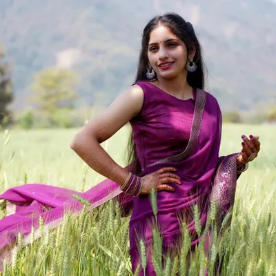 A bright and cheerful outdoor portrait in a field of wheat. The model's confident pose and smile, combined with the flowing purple saree, create a vibrant and lively lifestyle image.