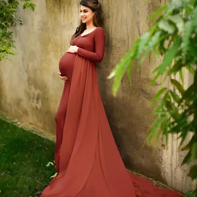 A beautiful outdoor portrait taken in a garden setting. The rich color of the red gown stands out beautifully against the natural green and earthy tones of the surroundings.