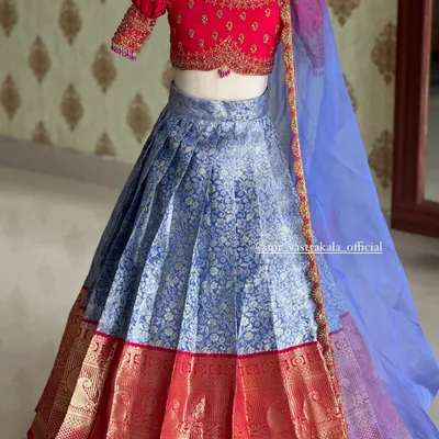 A beautiful kids' lehenga set, featuring a bright pink puff-sleeve blouse with delicate embroidery. The blue brocade skirt has a traditional silk border, and it's completed with a sheer blue dupatta.