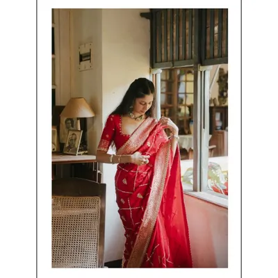 A stunning portrait of the bride-to-be in a vibrant red saree, standing by a vintage window. The soft natural light and classic setting create a timeless and graceful image.