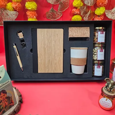 An elegant corporate Diwali gift set. This hamper includes a bamboo-finish diary and pen, a ceramic mug, and jars of premium dry fruits, all presented in a sleek black box.