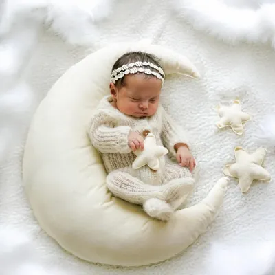 A sweet dream captured forever. This newborn girl, dressed in a cozy knit outfit and delicate headband, sleeps peacefully on our popular moon prop, creating a truly magical infant portrait.