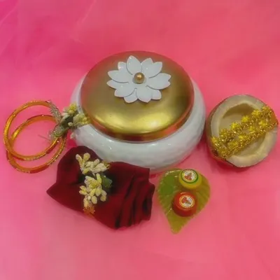 This white and gold metal box is a complete gift set. Here you can see the box alongside its contents: a blouse piece, bangles, coconut, and haldi-kumkum.