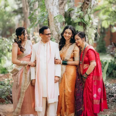 A beautiful family portrait taken in a lush garden setting during a wedding. The bride stands with her father, mother, and sister, all sharing a warm, happy moment together.