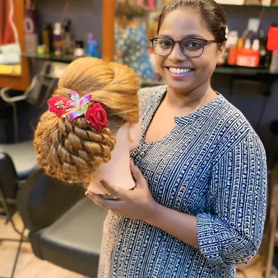 A happy student proudly displaying her finished bridal updo. She has masterfully created a twisted bun with floral accessories, ready for a real bride.