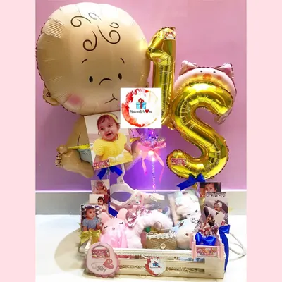 A grand first birthday hamper celebrating a baby girl, complete with "1st" foil balloons, personalized photos, and a crate filled with toys and goodies. This is a wonderful centerpiece gift for a milestone birthday.