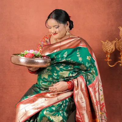 Draped in a magnificent green and red silk saree, this mom-to-be holds a traditional brass thali with flowers, creating a picture of grace and cultural reverence.
