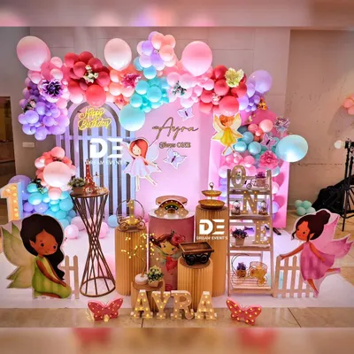 A fairy-themed first birthday party, complete with colorful fairy cutouts, a vibrant balloon arch, and custom light-up letters spelling the birthday girl's name.