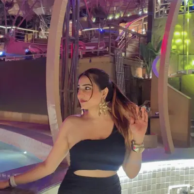 A sleek, one-shoulder black dress for a night out. The poolside setting and neon lights create a perfect party atmosphere.