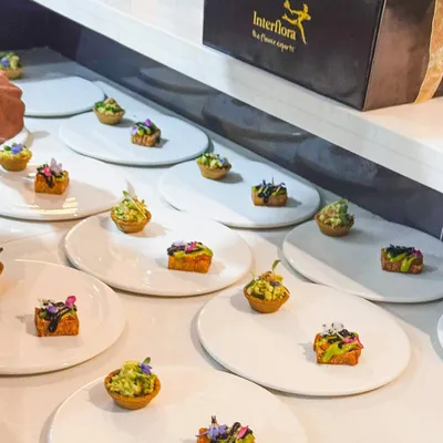 A wide shot of canapés being plated for a private event, in partnership with Interflora for the beautiful floral arrangements.