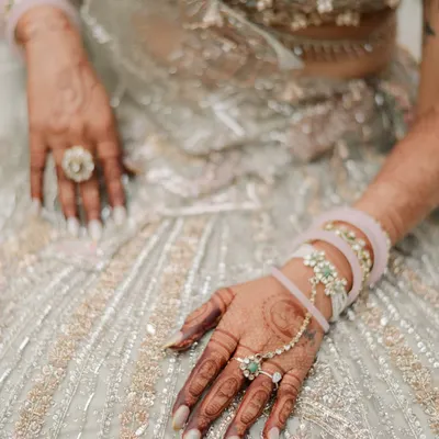 A close-up on the bride's hands, showcasing the intricate henna, the delicate hand jewelry, and the texture of her stunning lehenga. These details tell a story of tradition and personal style.