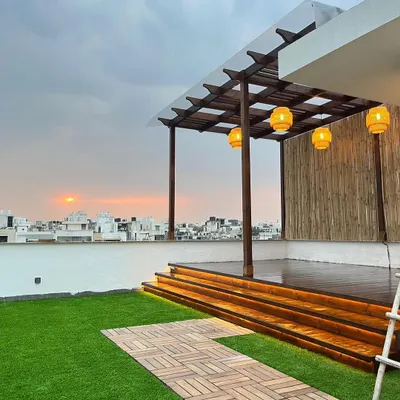 This is the finished rooftop, a perfect party place with a sunset view. The combination of the dark wood pergola, warm deck lighting, and green artificial turf creates an inviting atmosphere.