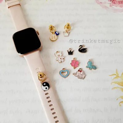 Make your smartwatch even smarter with these cute charms. This image shows a collection of enamel charms like a yin-yang, crown, evil eye, and teddy bear that can be attached to your watch band.