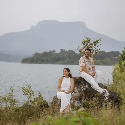 A stunning wide-angle shot of a couple seated by a tranquil lake, with a majestic mountain in the background. This showcases the epic scale of a destination pre-wedding shoot.
